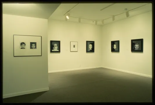 A row of black and white photographed portraits hang at eye level across the gallery wall. 