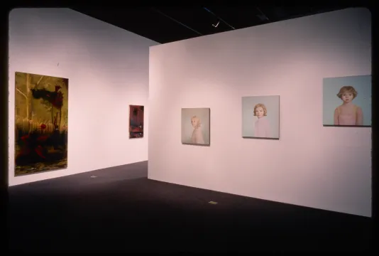 A gallery wall shows three pastel portraits while the opposing wall shows vibrant nature scenes.