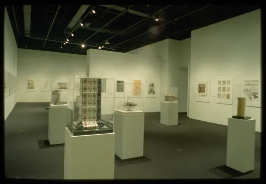 Architectural illustrations line the gallery walls. Models made from various materials sit on glass covered pedestals.