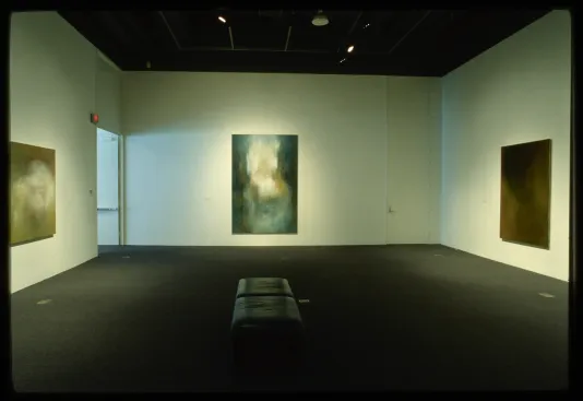 A bench sits in the center of the gallery for viewing the abstracted paintings around the room.