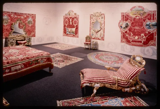 Red and white vintage carpets, furniture, chairs, and dressers fill a gallery room.