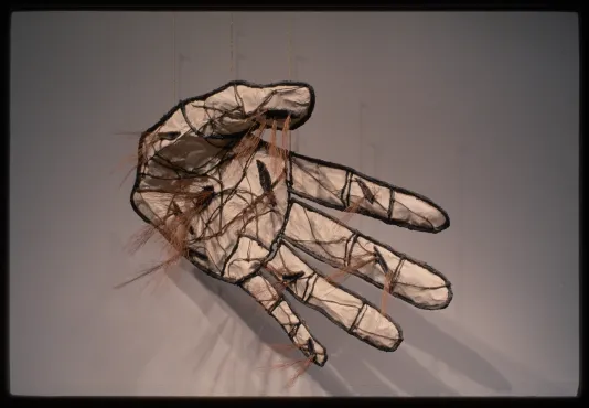 A sculpture of a hand is dangling away from the wall. Twigs make the outline while paper forms the hand. 
