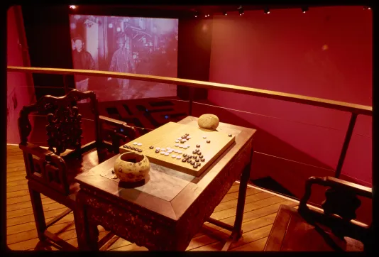 A game of goh is set up on a rafter above the gallery space. Below is a walkway and a projection on the opposing wall.