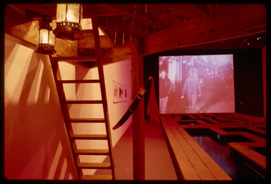 A ladder is set up to access the rafter. A covered knife is hung on the bar holding up the rafter while a projection plays. 