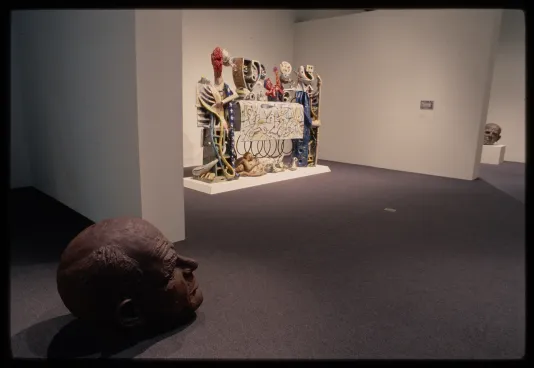 A sculpted head of Jackson Pollock rests on the floor with an abstract sculpture displayed beside it in the gallery. 