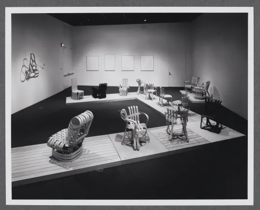 Bentwood chairs are arranged upon a wooden platform that makes its way through the gallery space. 