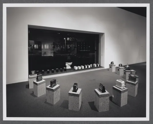A semi-circle of toasters on pedestals sit in front of the gallery window. Each toaster is a different model. 