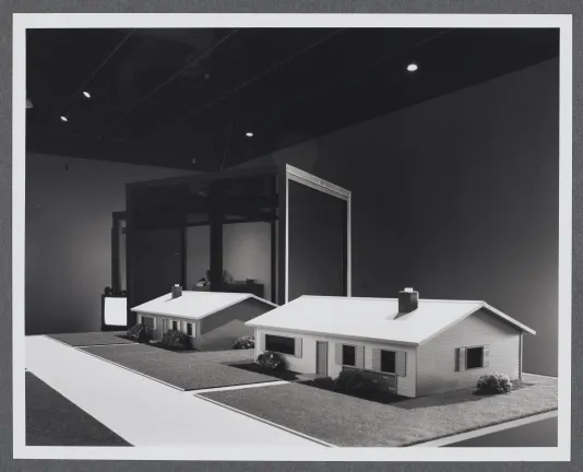 Architectural models of homes sit atop a pedestal while glass and mirror structures sit in the background.
