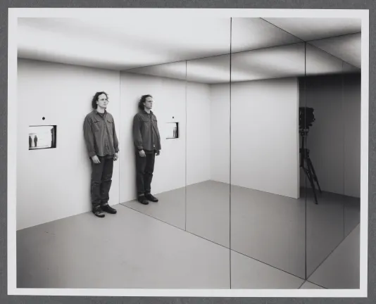 An installation with mirrors plays with perspective. A person stands beside a mirror as his reflection is cast beside them.