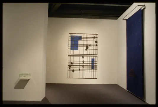 Small item in glass box on left, two large metal graphs with circles and blue shapes hangs in middle, large blue wall mural on right.