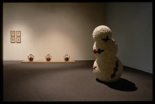 An installation view of The Masculine Masquerade. A snowman shaped sculpture stands in the foreground. 
