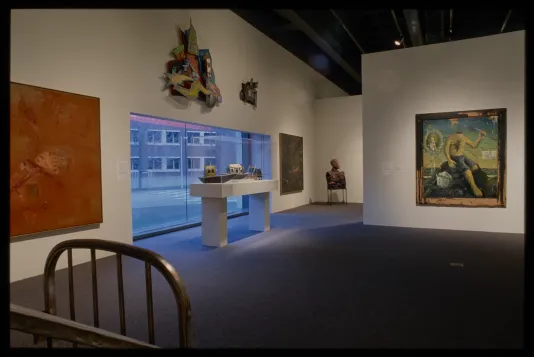 Paintings and sculptural works hang around the gallery window. A pedestal just in front of the window displays model ships. 