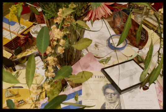 Seen from above, foliage of a floral arrangement hovers over a colorful surface strewn with stationery and other miscellany.