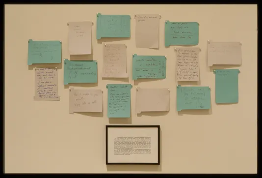 16 blue and white note cards with writing are randomly grouped on a wall, a small framed piece of text is centered below.