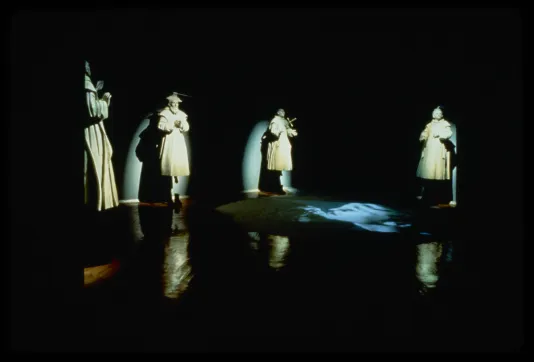 Four spotlit sculptures of saints in style of Cotan, in various pious positions with reflections and video projection on floor. 