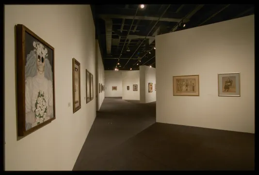 Framed paintings in a large gallery space. Nearest to the viewer is a painting of a skeleton in a bridal costume.