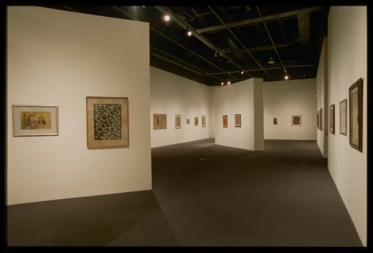 View of framed paintings hanging on the walls in a large gallery space.