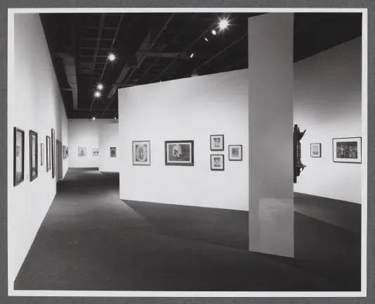 Black and white image of framed paintings hanging on the walls in a large gallery space.