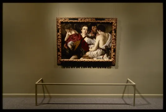 Caravaggio painting in gold frame of four musicians with slack expressions facing different ways wearing red and white togas.