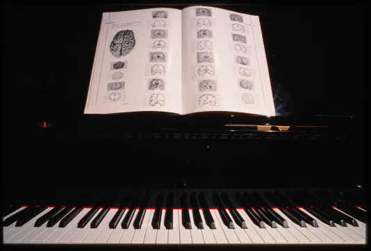 A book lies open with images of the human brain on the music rack of a black piano above a row of black and white keys.