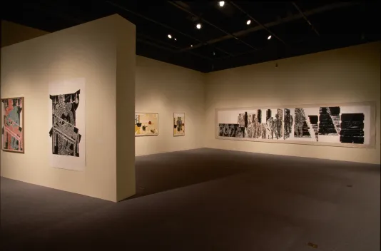 A long brown, black and white, framed, woodblock print spans the length of the back wall next to other prints in the gallery.