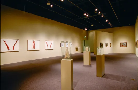 3 sculptures on slender pedestals in foreground surrounded by artworks on the walls of a large gallery.
