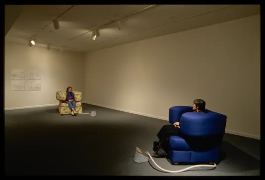 Two cushioned chairs are set across from each other. Each has large arms that squeeze the sitter between them.