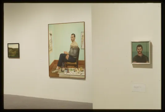 3 painting on a gallery wall - the large one inthe middle of a man seated in chair with a mint green background. 