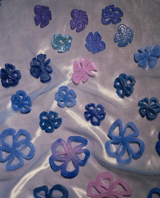 2 blue and 2 green, cast-glass flowers shapes on pink-cream shiny organza fabric.
