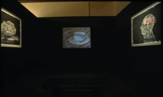 Drawing of a blue-tinted cup and saucer projected on a black wall is flanked on each side by black and white drawings.