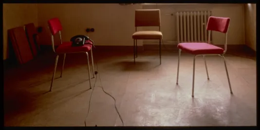2 red chairs and 1 organe chair in an empty room with a telephone on one chair. 