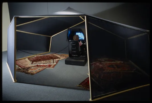 A tent like structure with rugs on the groun and a woman sitting at a game console inside.