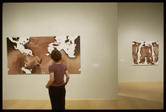 Woman looking at large abstract, brown work in gallery. 