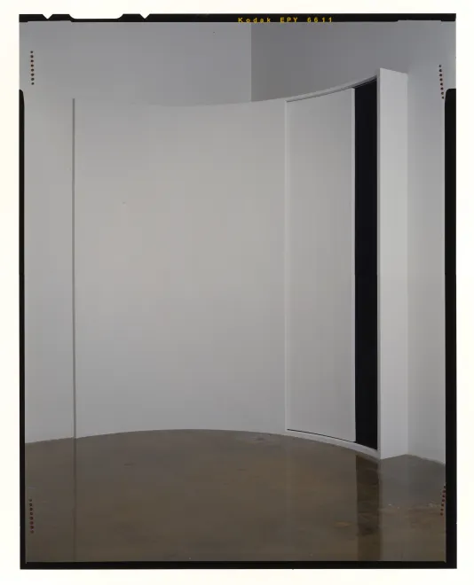 A shallow closet, partially open, set in a curved corner of a white room.