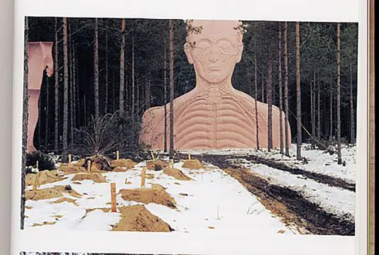 Amongst many trees sits a large outdoor sculpture of a man’s upper body and head. Snow and dirt lightly covers the foreground