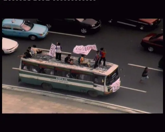 Standing on top of a bus, sitting amongst the traffic, are people waving signs in the air and looking all directions