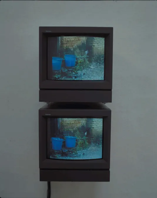 Mounted to the wall, one directly above the other, 2 box television monitors display the same image