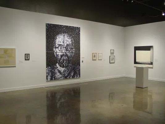 Large black and white portrait of a man centers on the gallery wall surrounded by smaller framed artworks