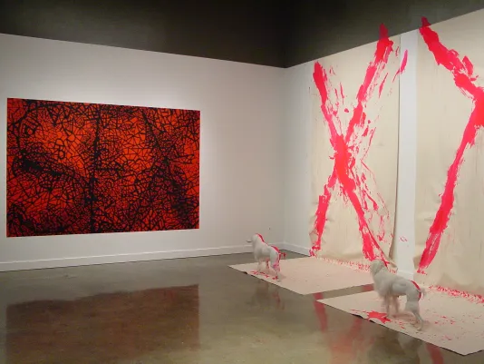 Large, abstract red and black artwork hangs to left of paint splattered canvases and statues on right gallery wall