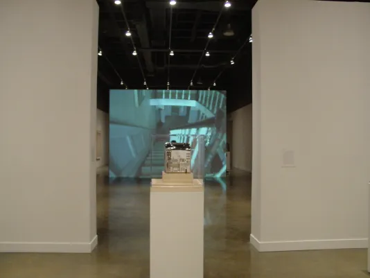 2 white walls give way to a large video projection in the back room, with a vitrine holding a small object in the foreground
