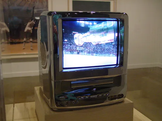 Close up photograph of a miniature chrome television, displaying a sports event.