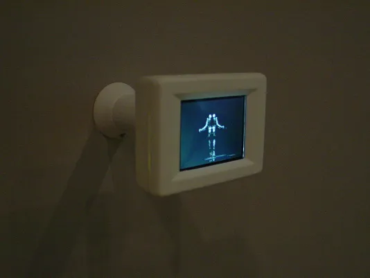 Small, white framed digital screen is mounted to the wall, displaying a white human-like form on a black background