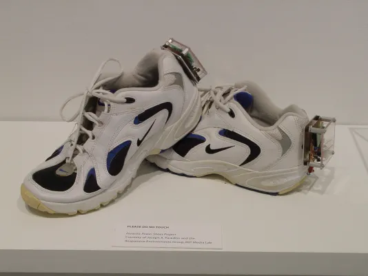 White nike sneakers with black and blue detailing and a clear box filled with electronic wires attached to each heel