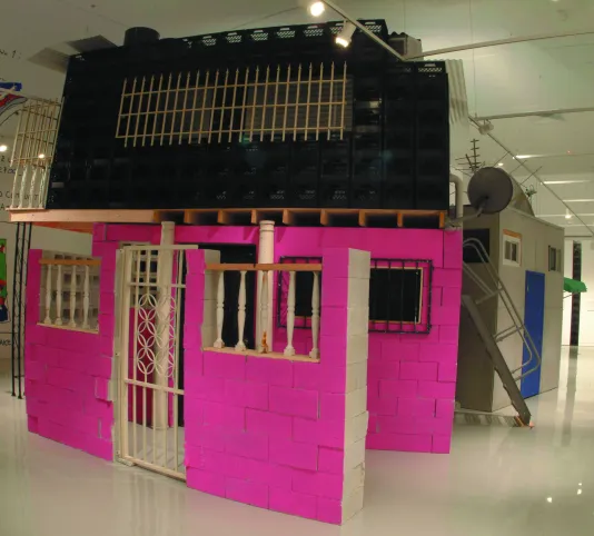 A gallery space filled with built structures made from various materials, one painted green, the others pink and black