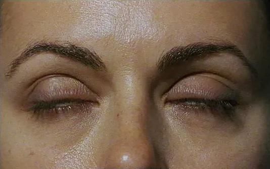 Video still captures a close up view of a woman mid-blink, exploiting the texture of her fair skin and dark eyebrows