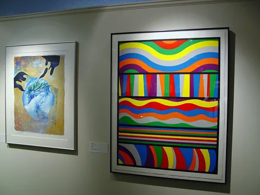 wo framed artworks hung on a wall, one is a bright multicolored print of different shaped lines and the other is a portrait.