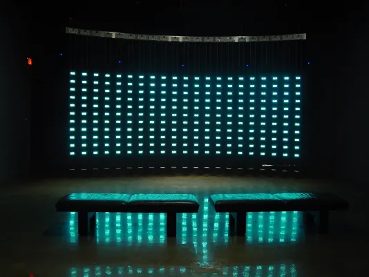 In a dark room, two benches are illuminated in front of hundreds of miniature, glowing digital screens