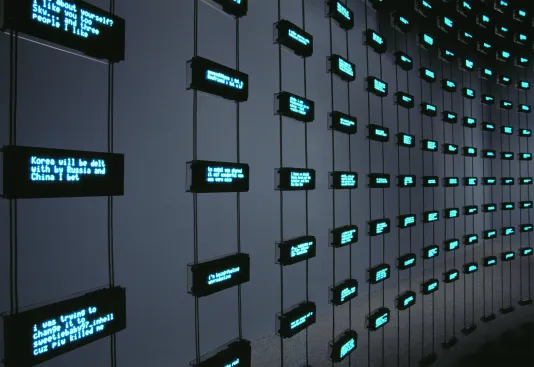 Several small digital screens, displaying blue text, hang by copper wire in evenly spaced rows and columns.
