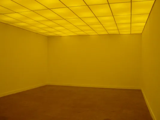 An empty room glows yellow, lit from a tiled ceiling.