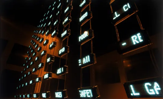 Miniature digital screens displaying blue text, hang in a grid in a dark room